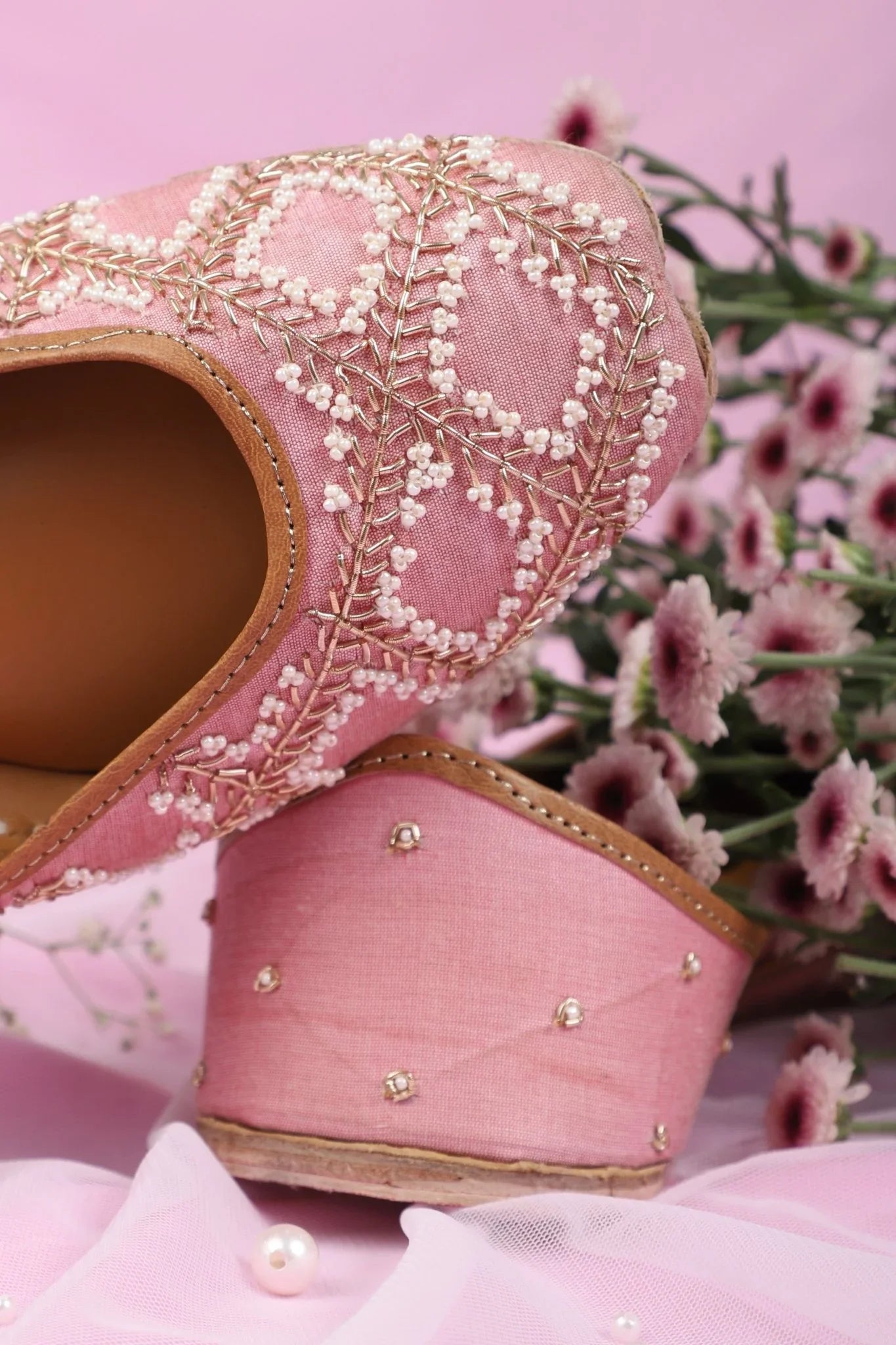 Close-up of pink women's jutti with pearl and bead embroidery on pink background with flowers